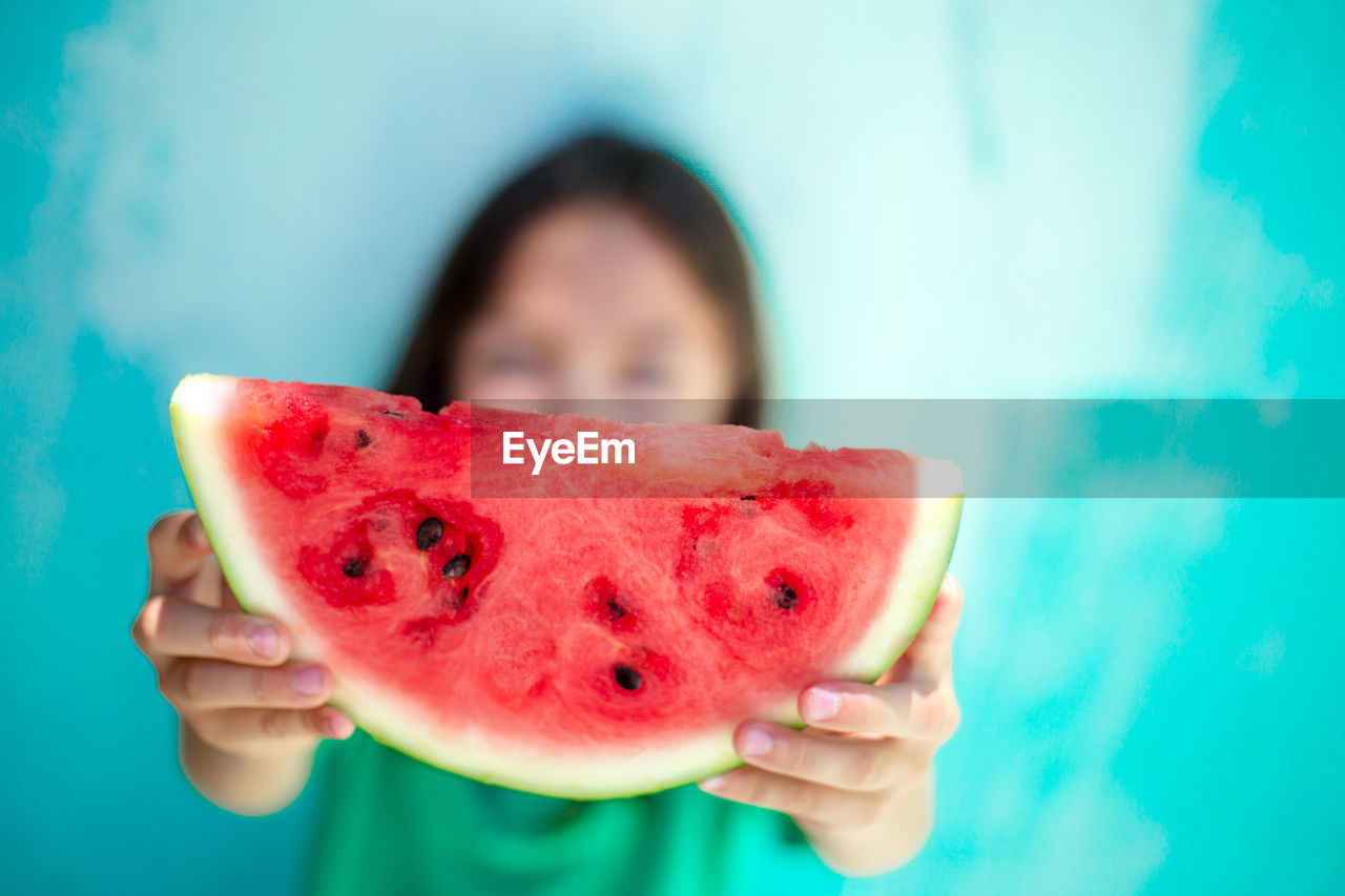 Close-up of girl holding watermelon slice against blue wall