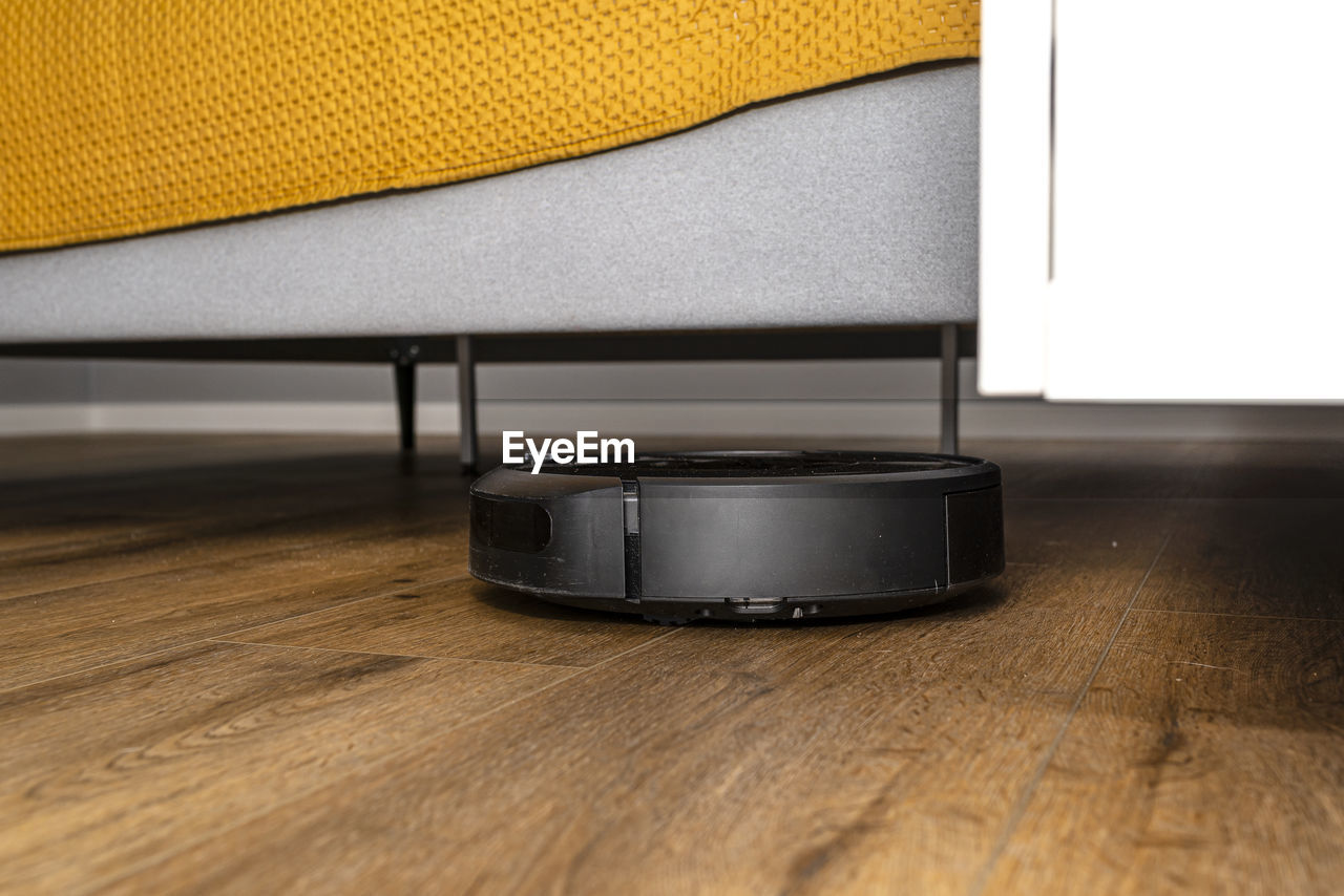 A modern robotic vacuum cleaner cleans vinyl panels under bedroom furniture. 