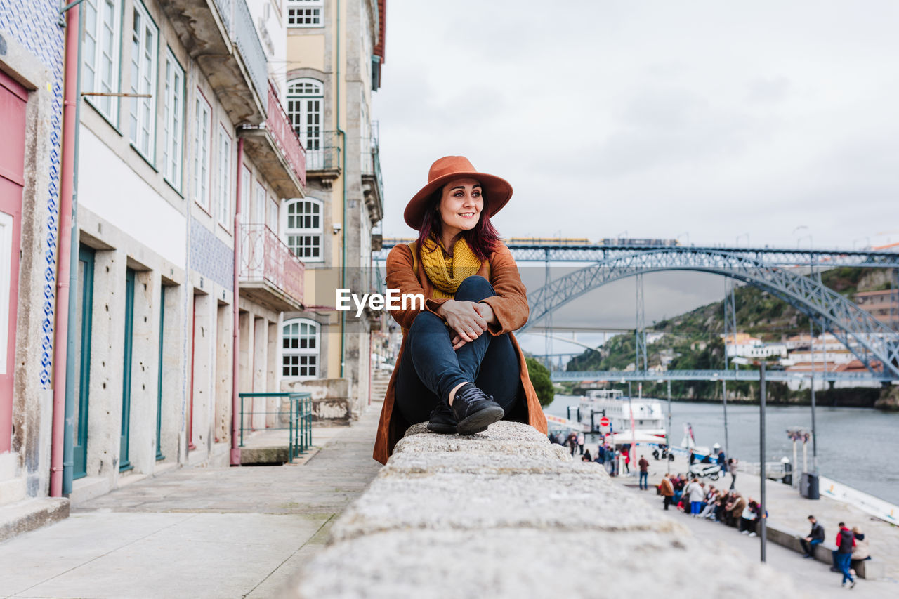 Portrait of young woman on retaining wall in city