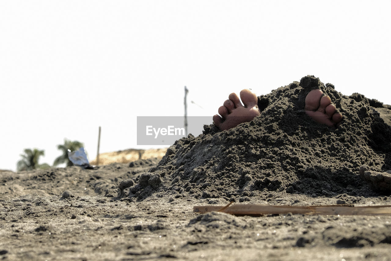 Low section of person on sand against clear sky