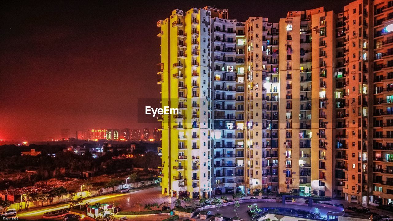 ILLUMINATED BUILDINGS BY ROAD AGAINST SKY IN CITY