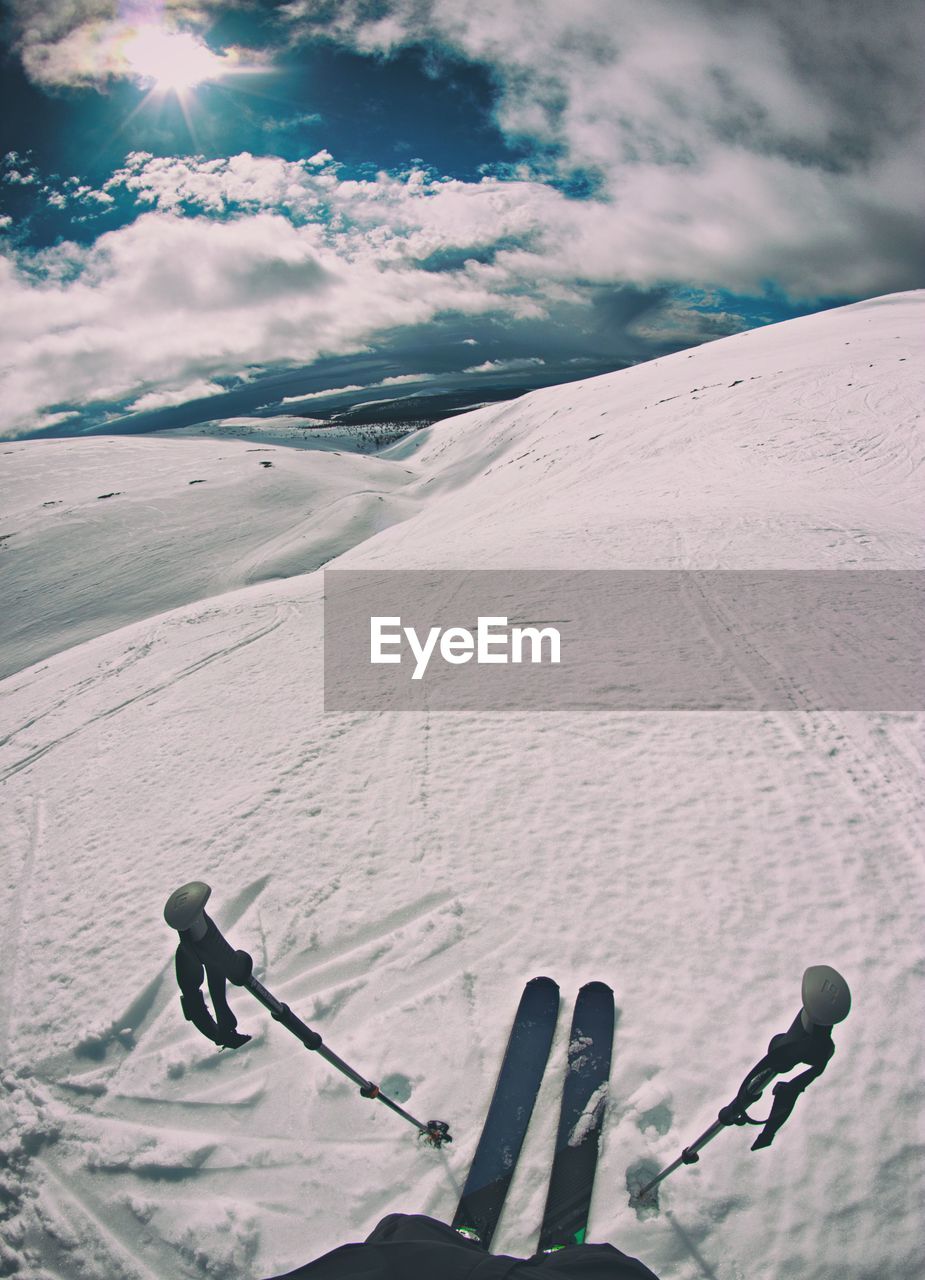 Low section of person skiing on snowcapped mountain against cloudy sky