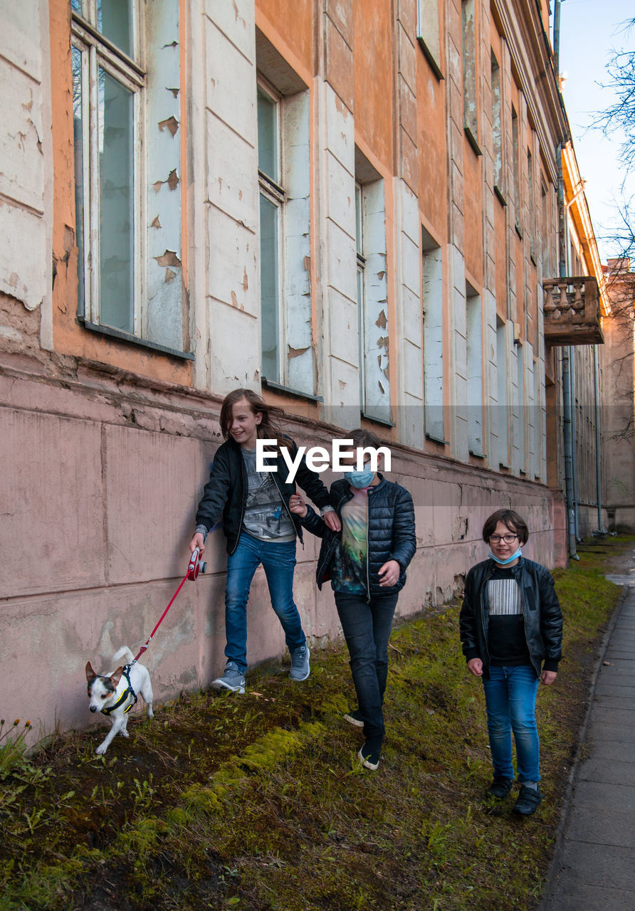 Full length of the three boys walking with dog near building