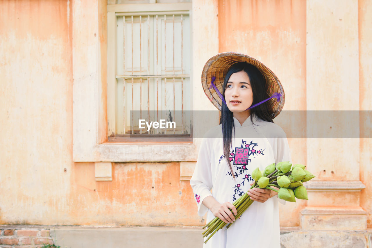 Portrait of young vietnamese woman standing against house