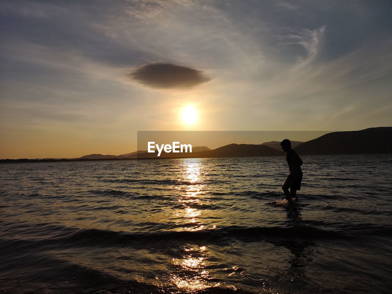 Silhouette boy wading in sea against sky during sunset