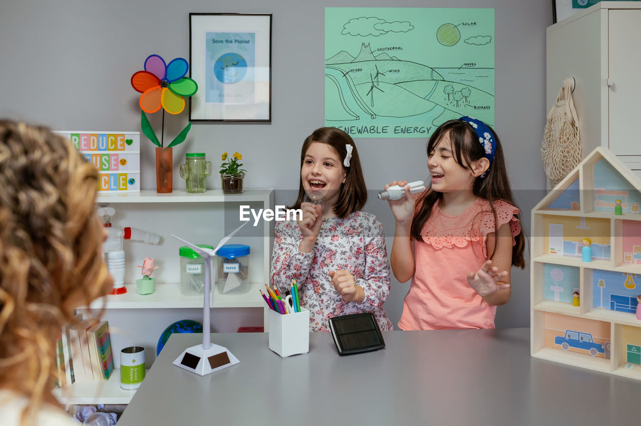 Female students singing using light bulbs as microphones in ecology classroom