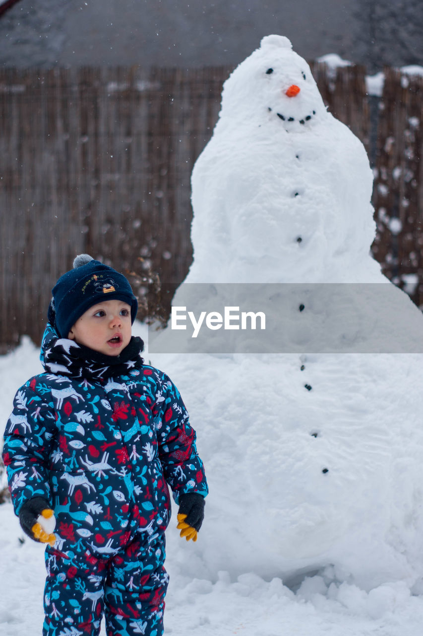 Cute boy standing against snowman