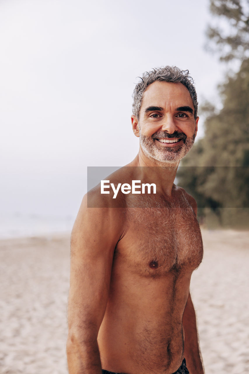 Portrait of smiling shirtless man standing at beach on vacation
