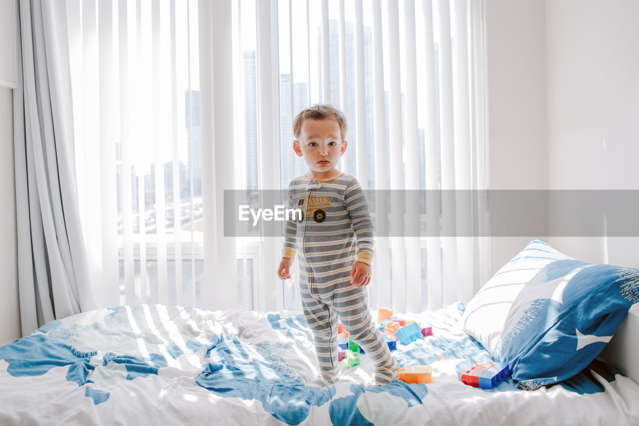 Boy toddler standing on bed in room at home and looking at camera. adorable innocent baby 