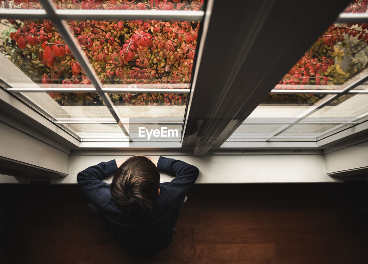 Young boy sitting on floor looking out window from high angle