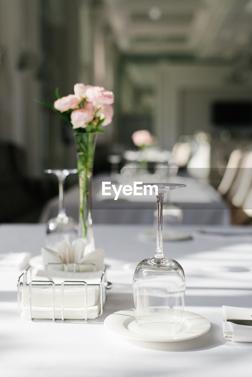 flower, flowering plant, table, plant, setting, furniture, centrepiece, place setting, arrangement, household equipment, elegance, freshness, vase, indoors, glass, dining table, flower arrangement, nature, decoration, beauty in nature, no people, bouquet, drinking glass, food and drink, white, plate, luxury, wedding, wine glass, domestic room, crockery, focus on foreground, celebration, wealth, kitchen utensil, home interior, flower head, dining room, restaurant, eating utensil, event, rose, tableware, seat, tablecloth, porcelain, wedding reception, selective focus, chair, domestic life, rehearsal dinner, business, drink, ceremony, still life, napkin, fork, lighting, love, lifestyles, centerpiece