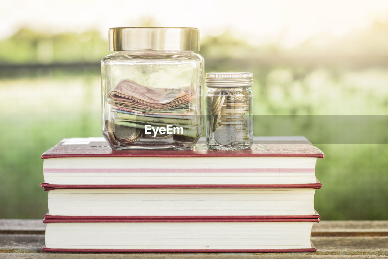 Close-up of currency in jars on stacked books at table