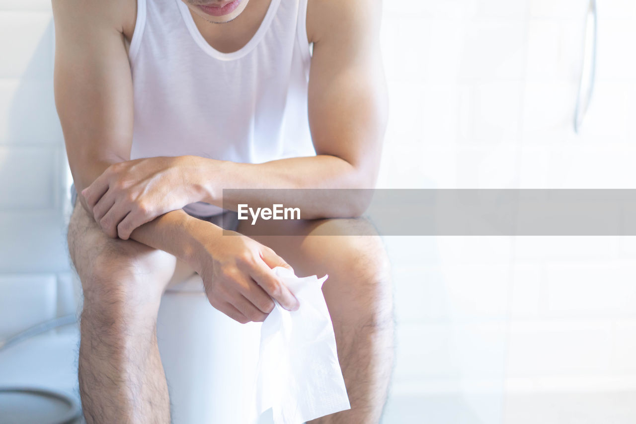 Midsection of man sitting on toilet at home