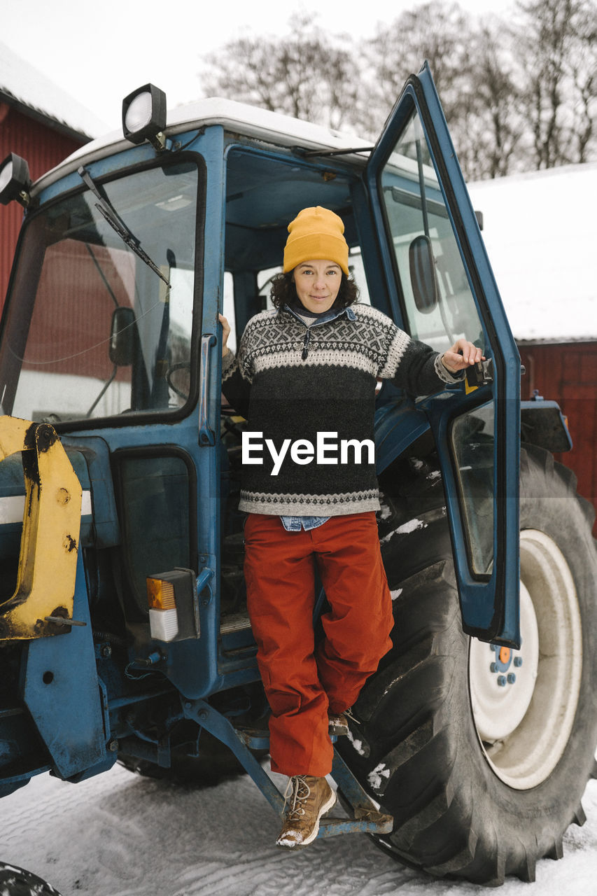 Full length of mature woman disembarking from tractor during winter