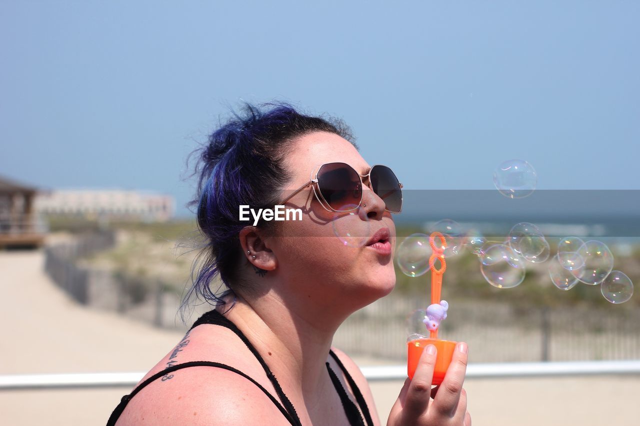 Young woman blowing bubbles at beach against sky