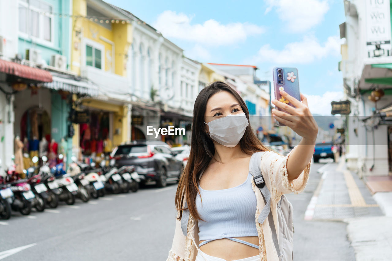 Asian traveler wearing a medical mask take a photo while walking in old town phuket, thailand. 