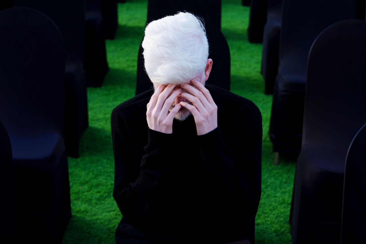 Portrait of an albino man with hands over his eyes sitting on the chair