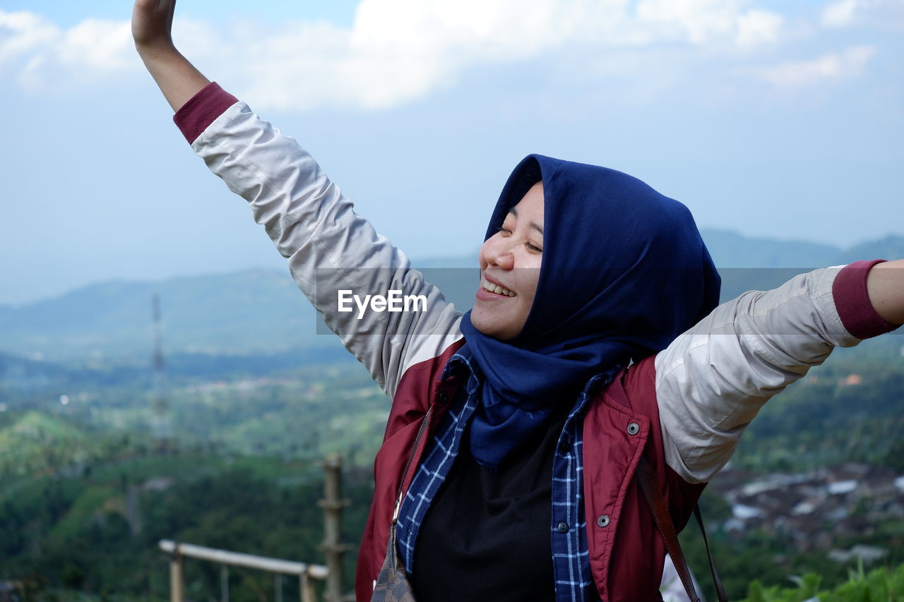 Rear view of woman with arms raised standing against sky