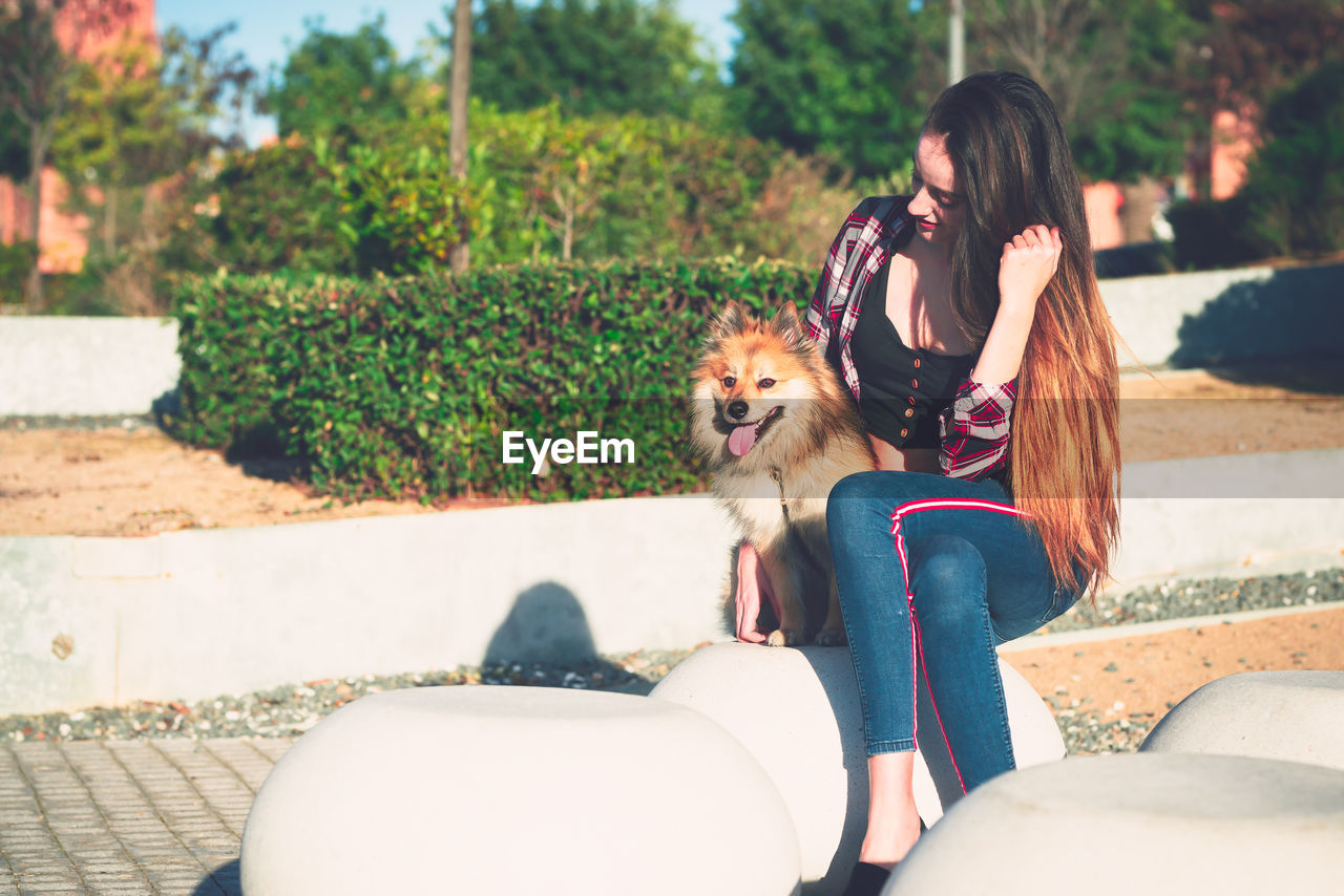 Woman sitting with dog at park during sunny day