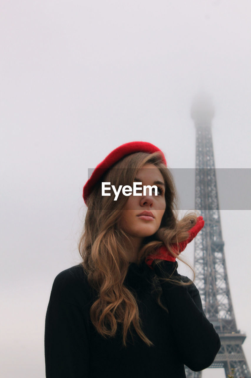 Portrait of young woman standing against clear sky and eiffel tower