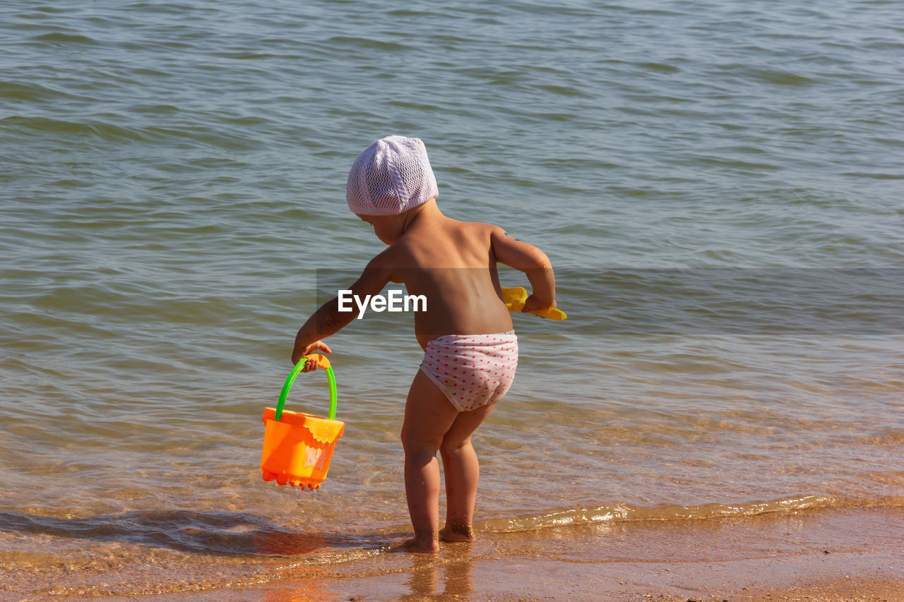 REAR VIEW OF SHIRTLESS BOY STANDING IN WATER