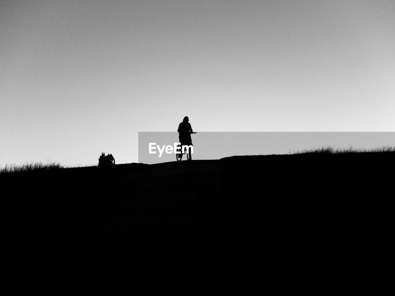 Silhouette man bicycling on field against clear sky
