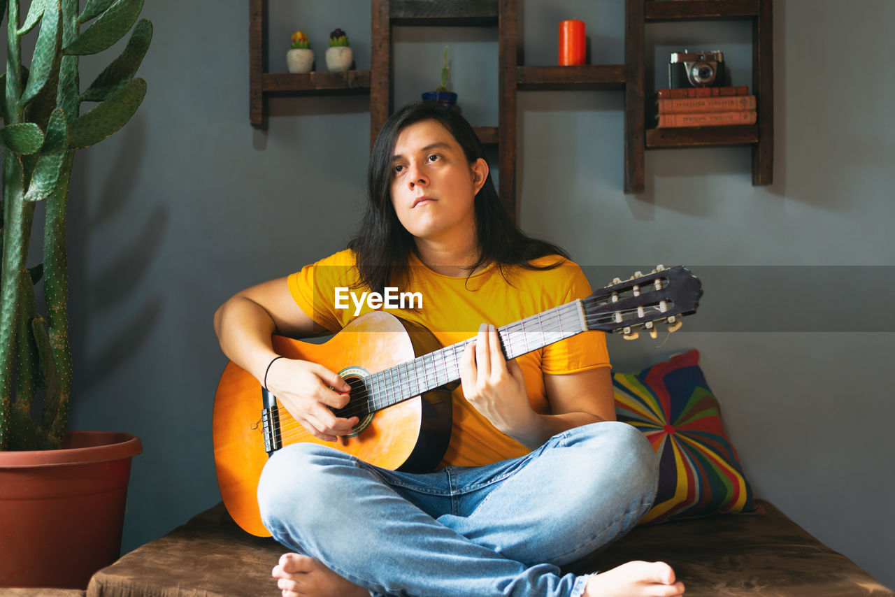 Man with long hair playing guitar at home in chill place pandemic time