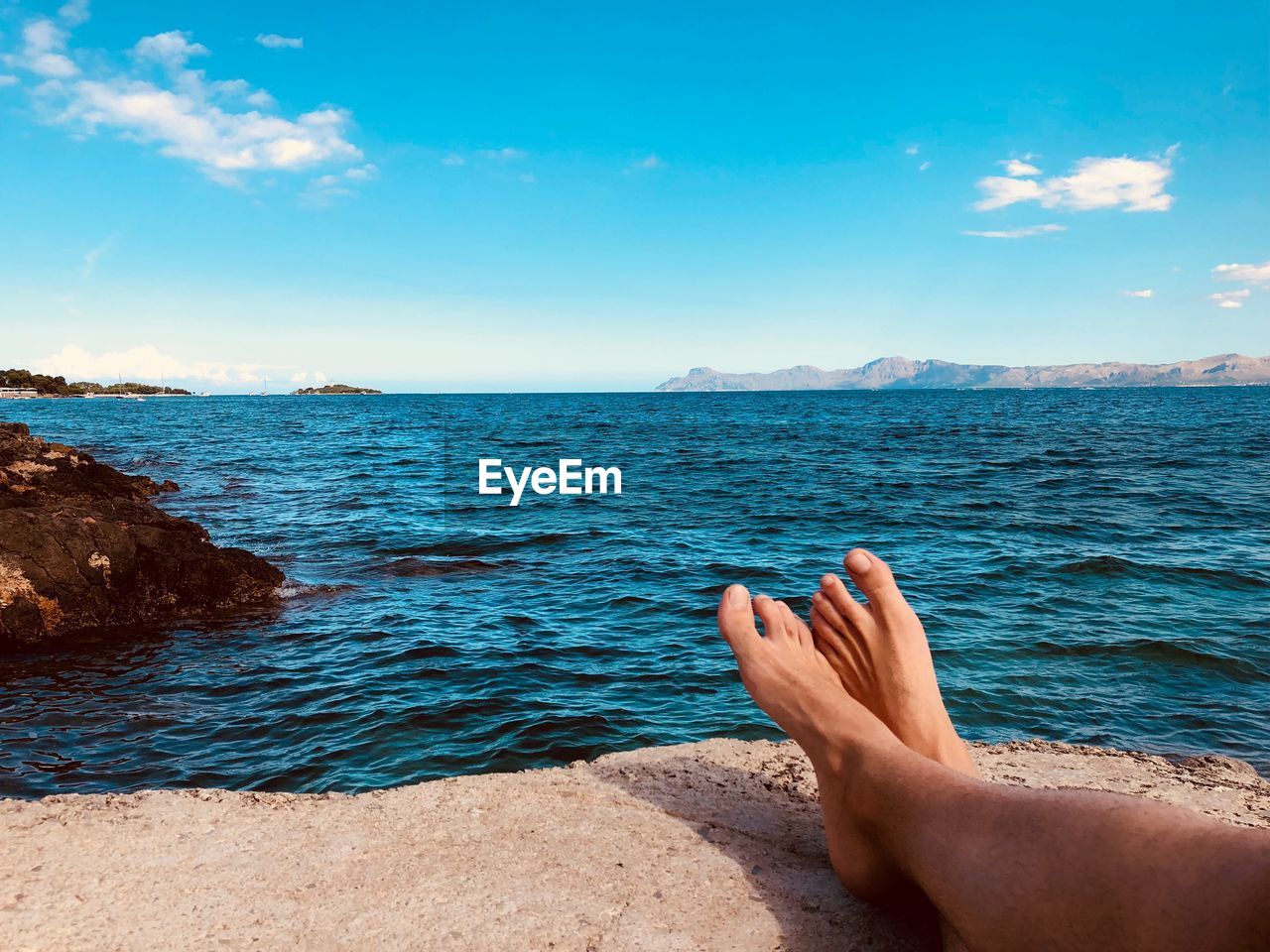 Low section of man wearing shoes while sitting at beach against sky