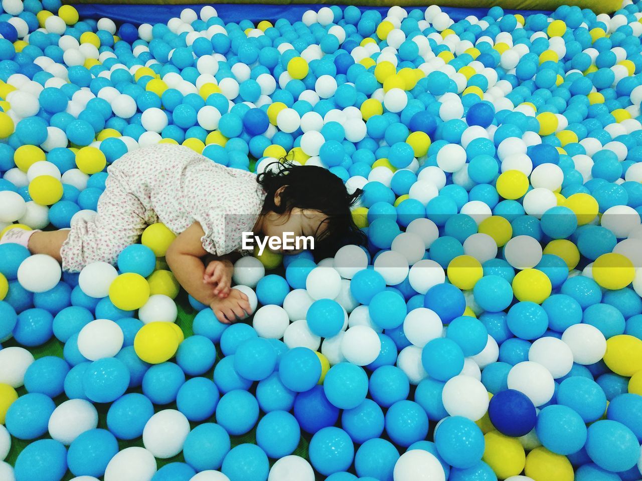 High angle view of baby girl lying on multi colored balls