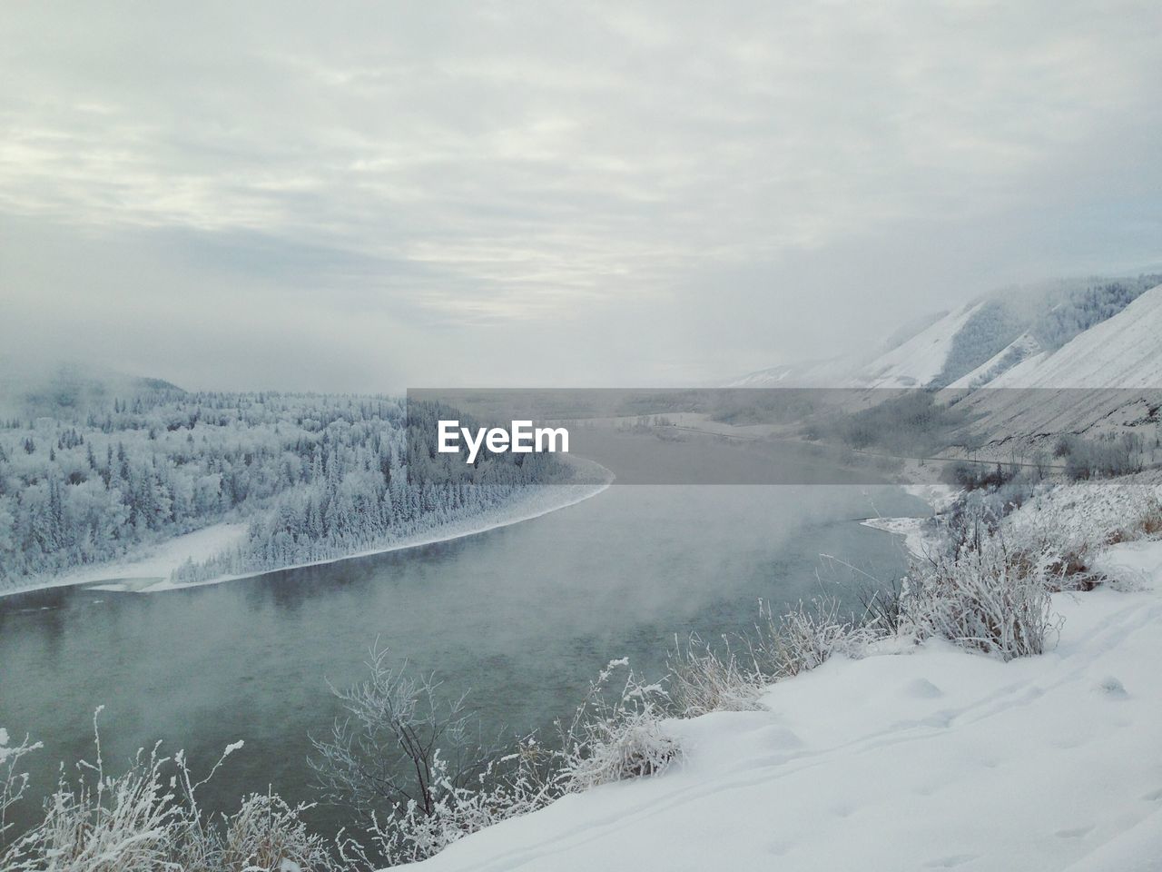 Scenic view of river by snowcapped mountain against cloudy sky