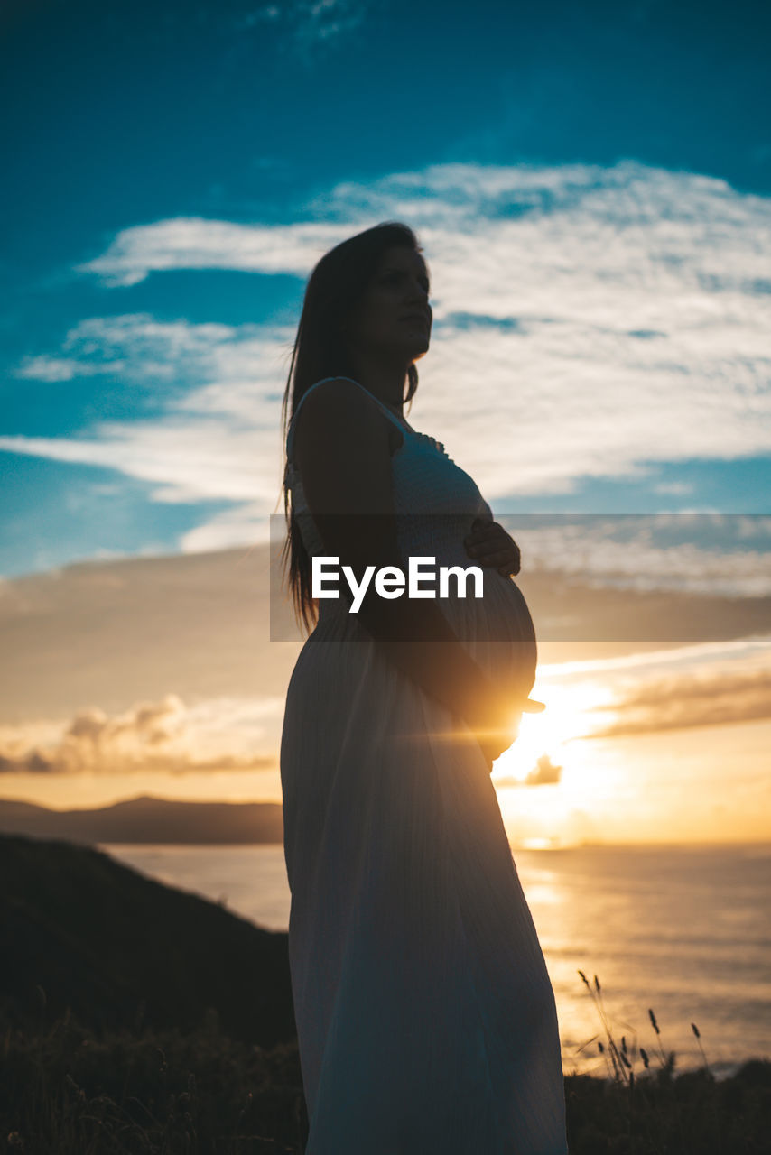 Side view of pregnant woman standing sky during sunset
