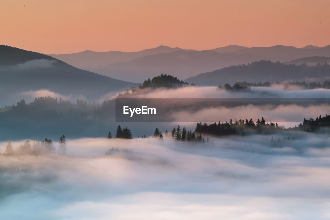 Scenic view of fog covered mountains against sky during sunrise