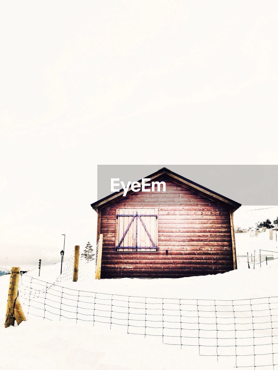 Fenced lone house on snow landscape against clear sky