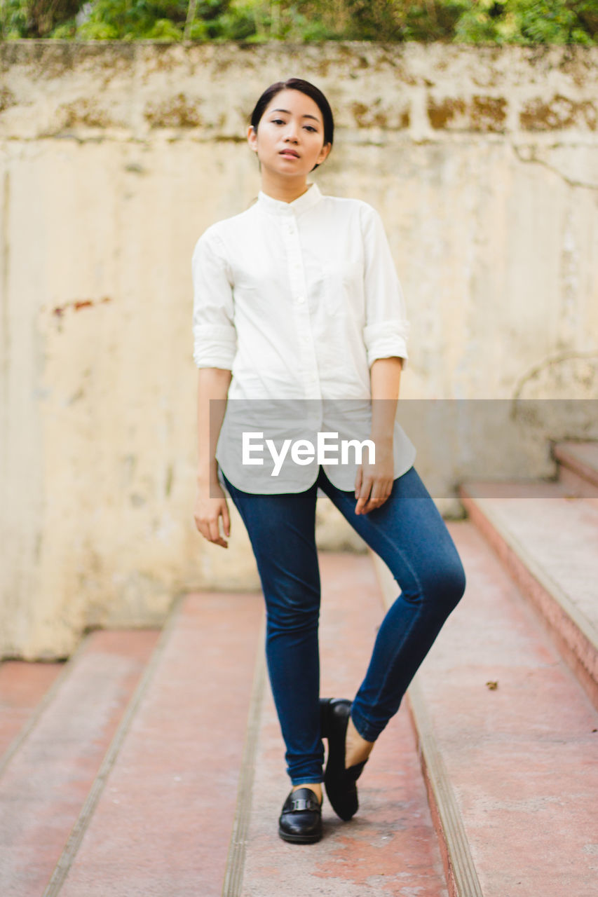 Full length portrait of woman standing on steps against wall