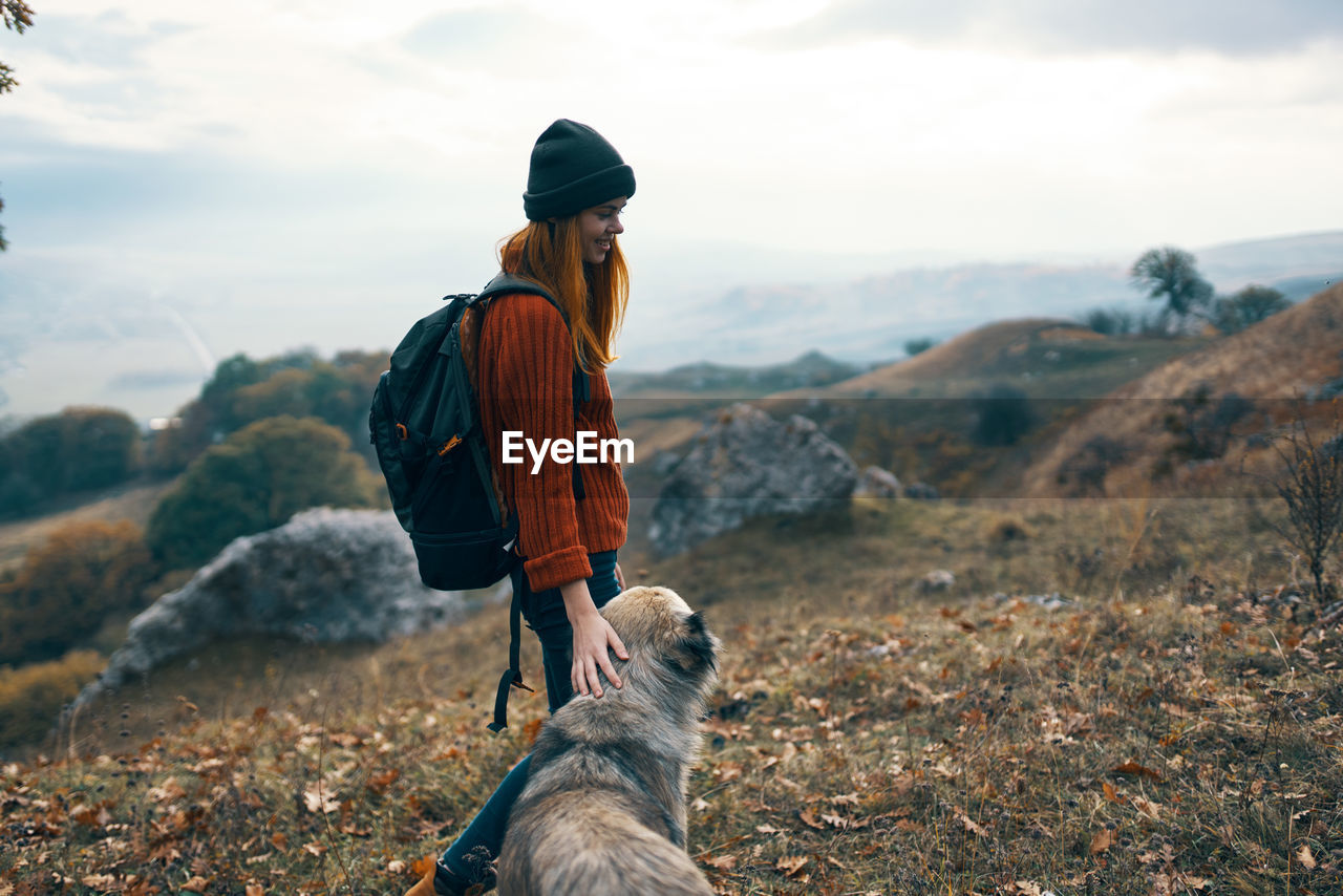 REAR VIEW OF WOMAN WITH DOG AGAINST SKY