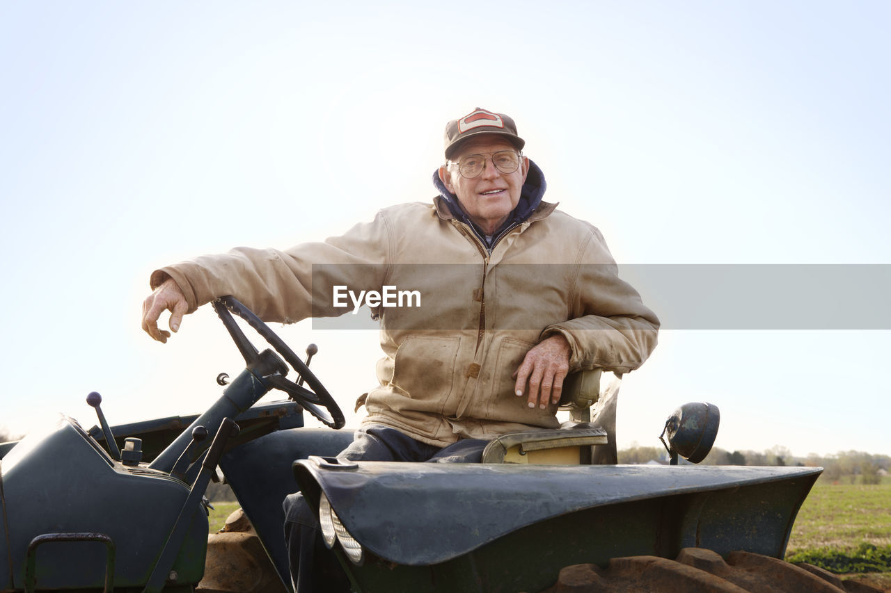 Portrait of confident farmer driving tractor against sky
