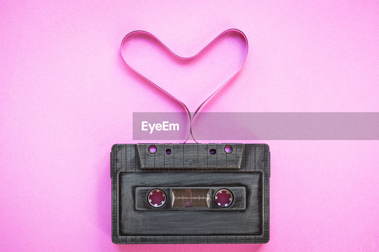 Close-up of gray audio cassette with heart shape against pink background