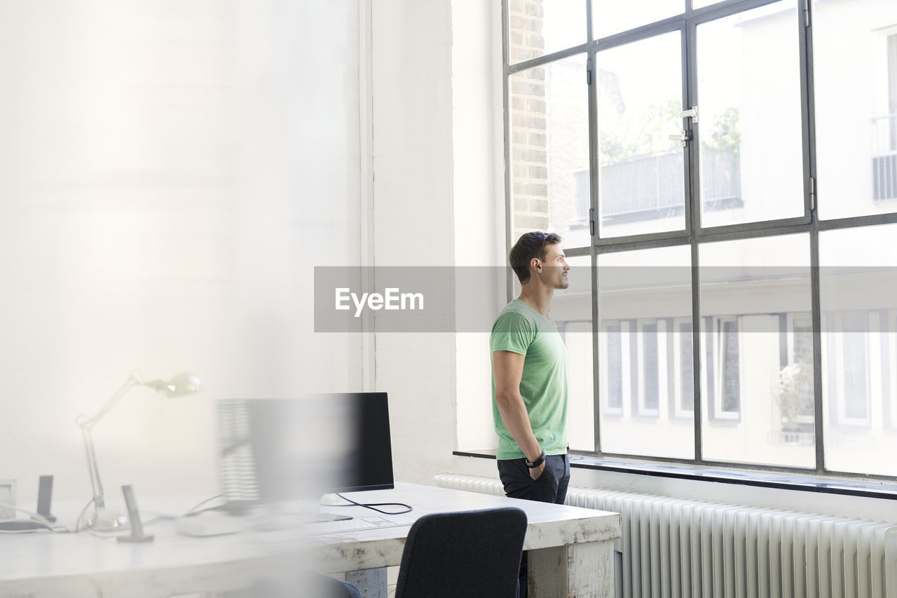 Young businessman looking out of office window, looking pensive