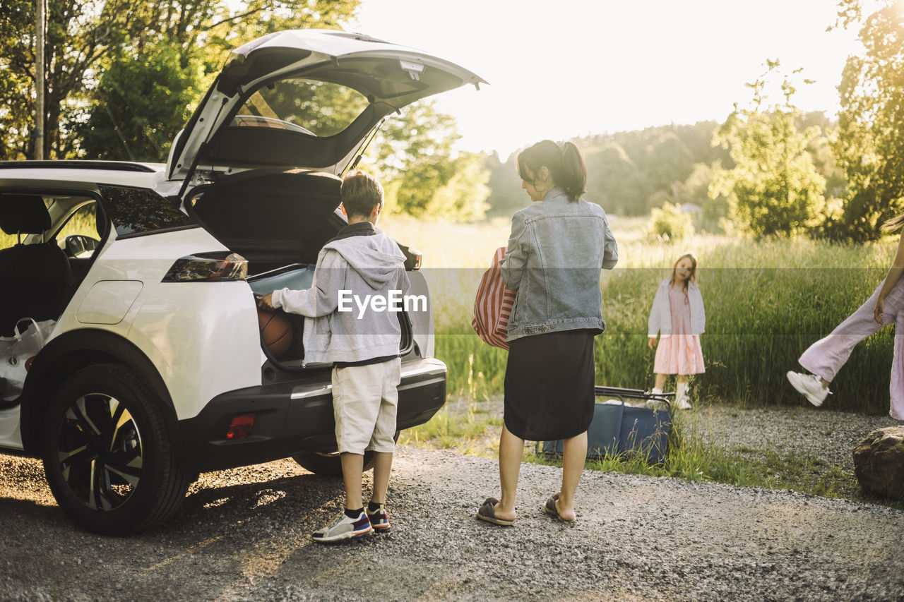 Son and mother unloading luggage from car trunk