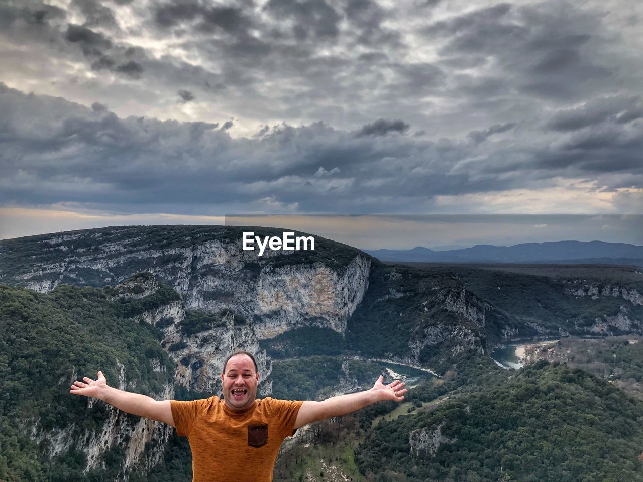 Portrait of mid adult man with arms outstretched standing on observation point against mountains