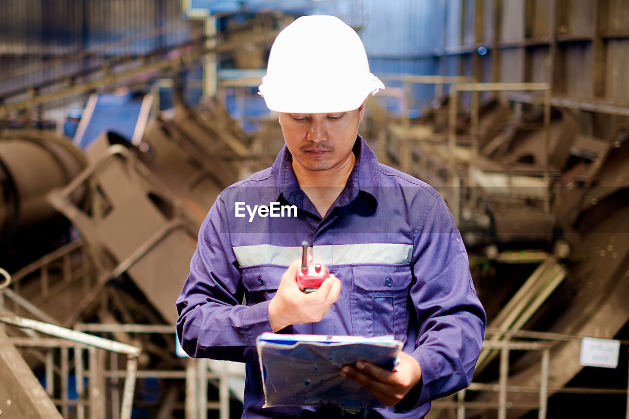 Engineer looking at walkie-talkie while standing in workshop