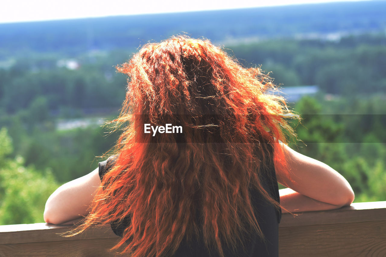 Rear view of woman leaning on railing against green landscape