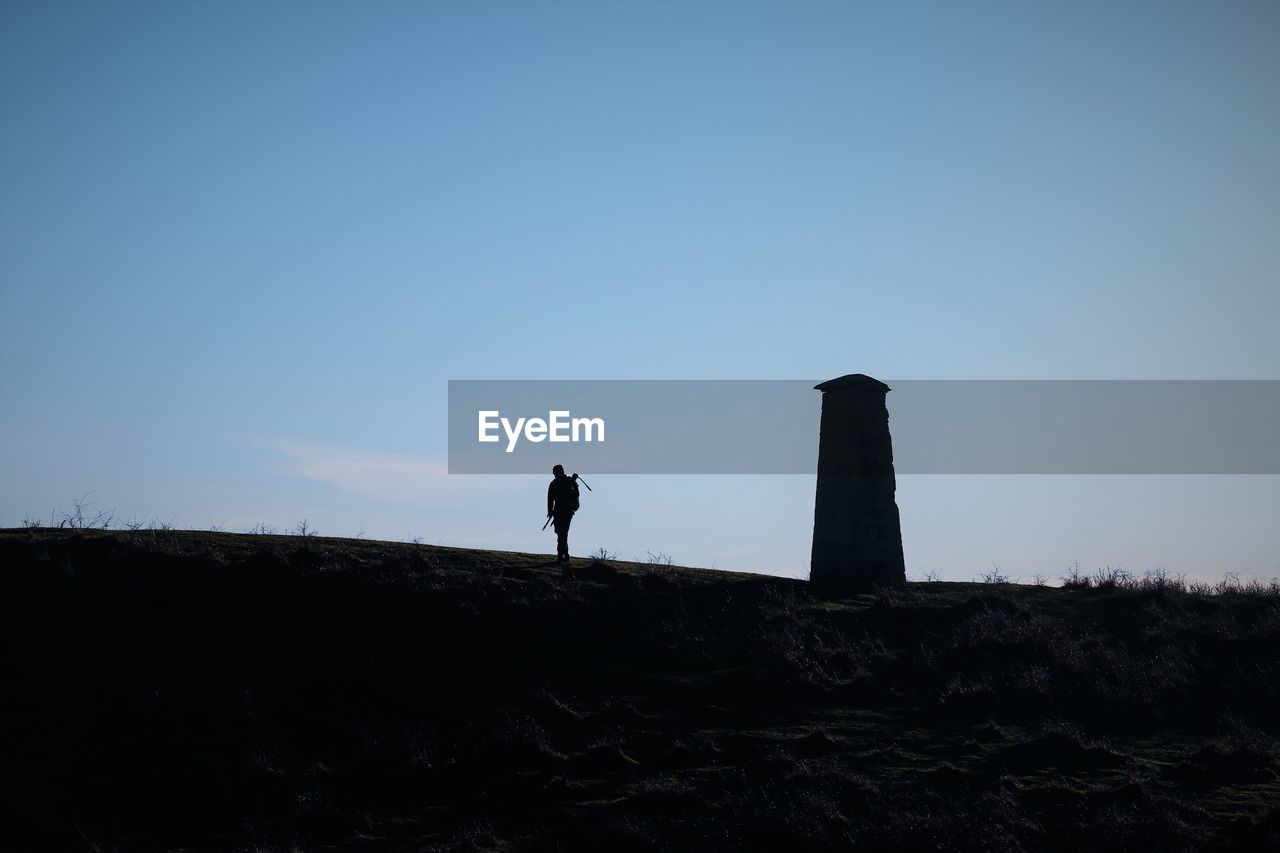 Silhouette photographer standing on a hill biside a tower against clear sky