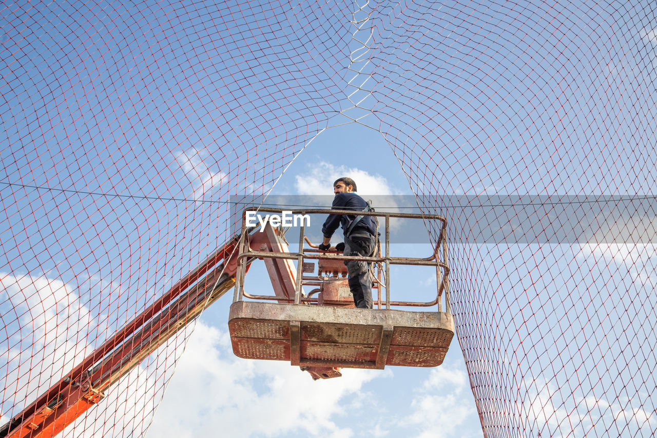 Low angle view of man working while standing on crane