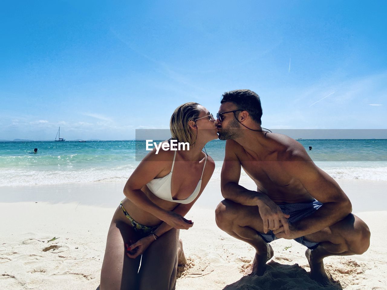 Couple kissing at beach against blue sky