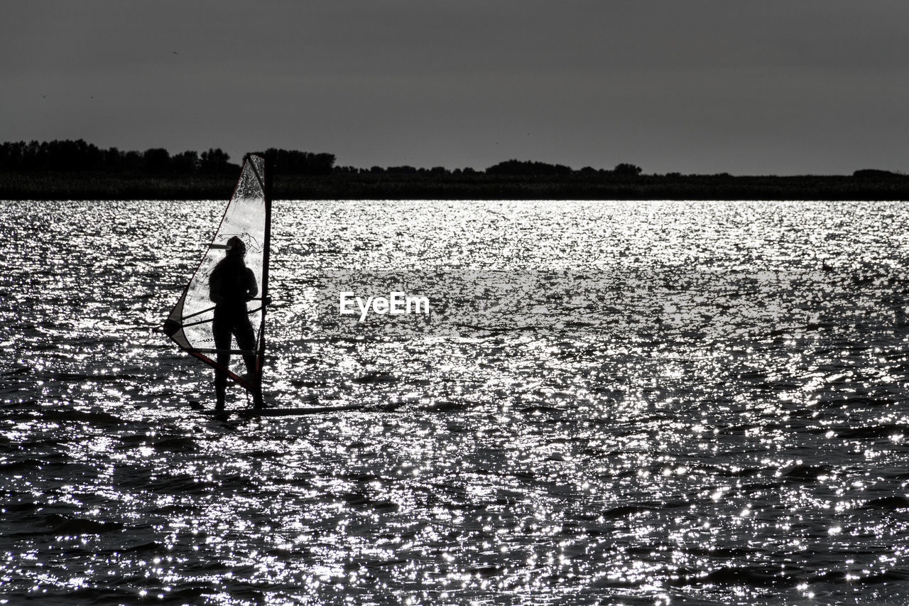 SILHOUETTE MAN STANDING BY LAKE AGAINST SKY