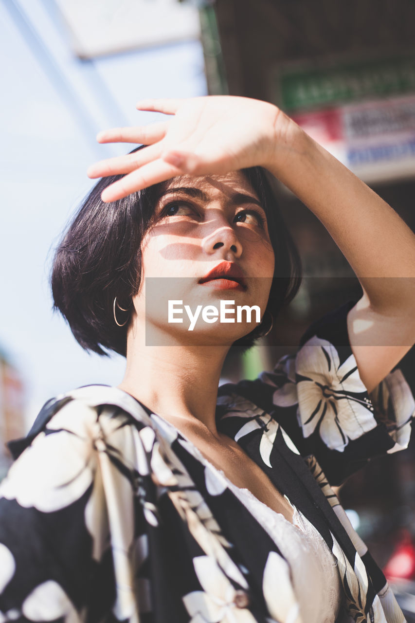 Woman looking away while shielding eyes in city