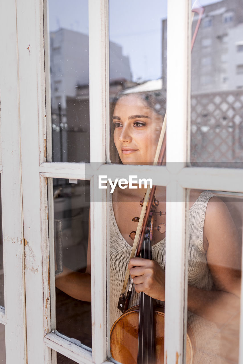 Young girl through a window while holding a musical instrument.