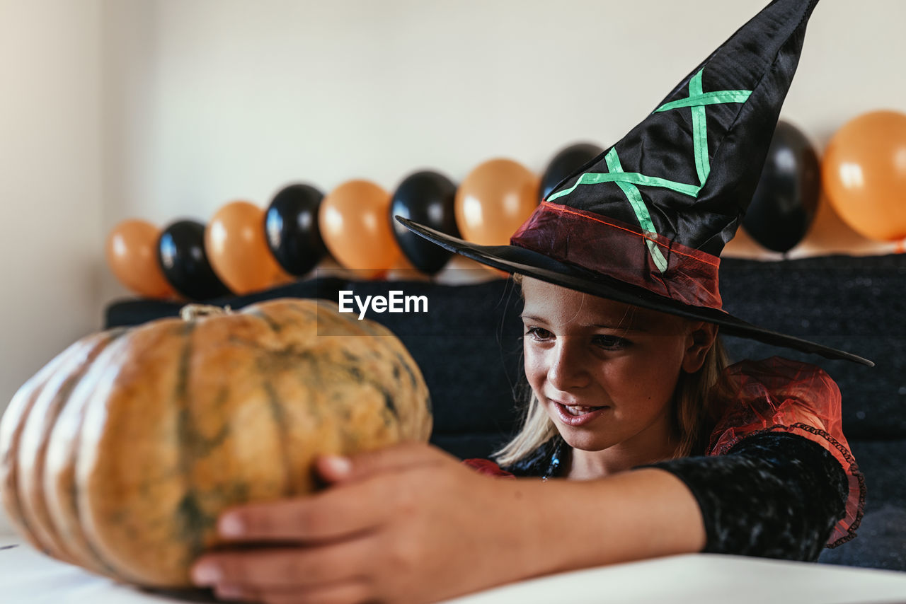 Girl in costume holding pumpkin on table