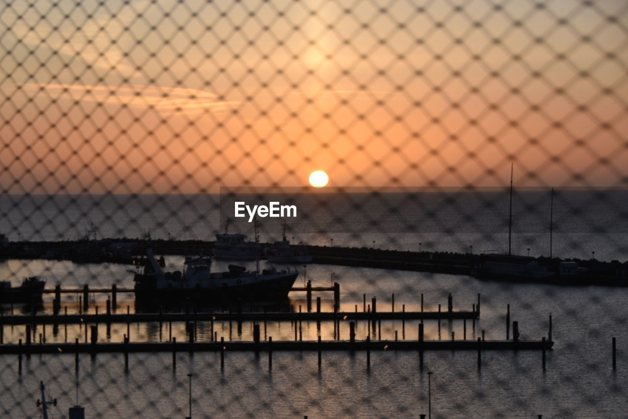 High angle view of silhouette boat at harbor seen through fence